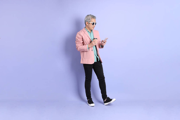 Der erwachsene asiatische Mann der vierziger Jahre stolziert auf dem lila Hintergrund mit smarter Freizeitkleidung herum. - Foto, Bild