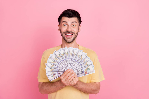 Photo of astonished lucky positive man wear stylish yellow clothes hold usd rejoice impressed success isolated on pink color background. - Foto, Imagen