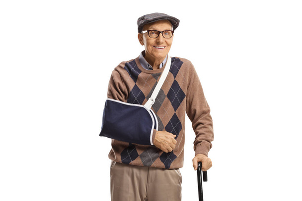 Smiling elderly man with a broken arm wearing a splint and standing with a cane isolated on white background - Φωτογραφία, εικόνα