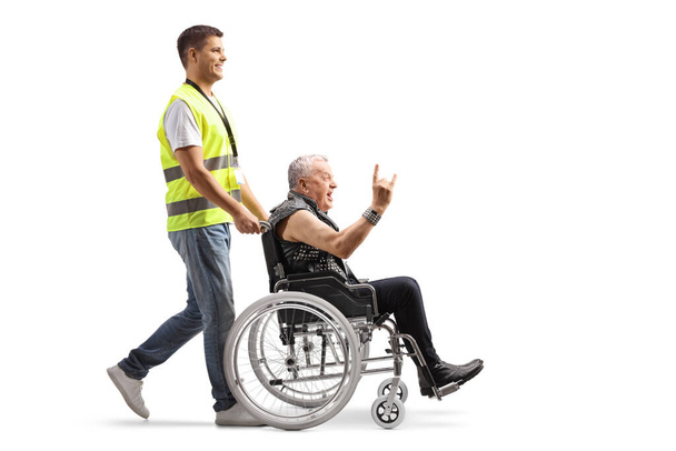 Pełny profil pracownika społecznego pchającego punka na wózku inwalidzkim odizolowanego na białym tle - Zdjęcie, obraz
