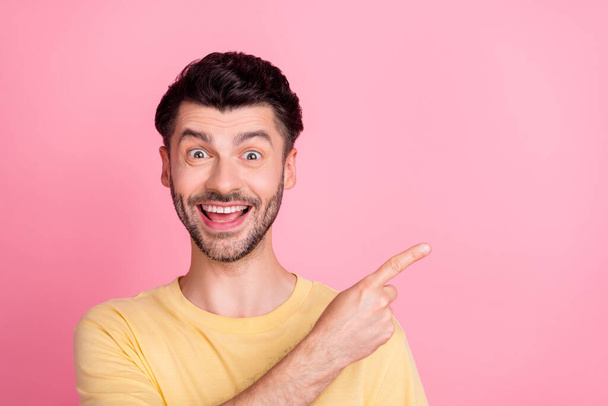 Portrait of ecstatic positive crazy man with stylish haircut wear yellow t-shirt directing empty space isolated on pink color background. - Fotó, kép