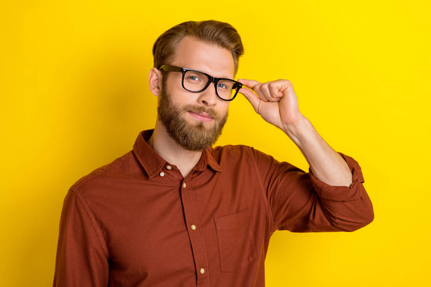 Portrait of cheerful satisfied handsome man with masculine beard burgundy shirt hand touching glasses isolated on yellow color background. - Photo, image