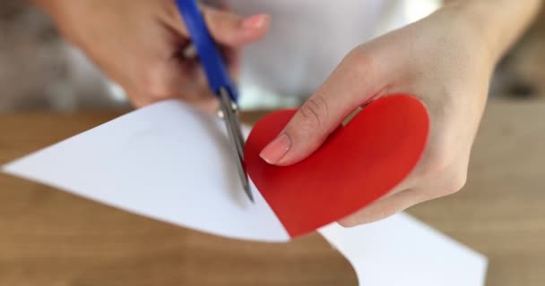 Tyttö leikkaa sydämen ulos punaisesta pahvista sakset koristeluun. Ystävänpäivän valmistelu - Materiaali, video