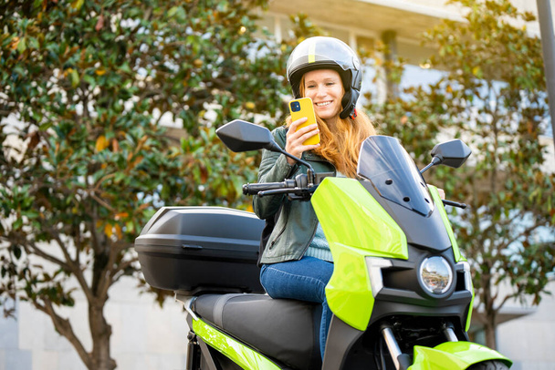 Portrét rudovlasé ženy na motocyklu pomocí smartphonu - Fotografie, Obrázek