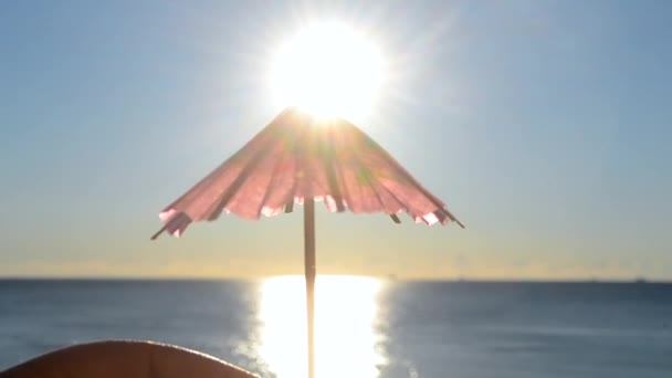 Чоловік тримає в руках одну червону паперову парасольку коктейль прикраси на тлі блакитного неба, яскраво сяючого сонця і сонячного шляху на поверхні блакитного моря. Концепція літа, моря, відпочинку, туристичного туризму
 - Кадри, відео