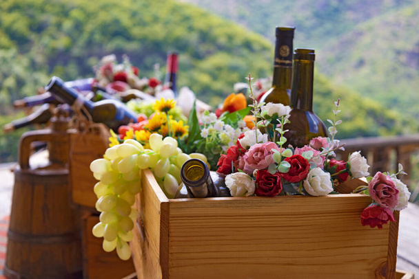 Caja de madera con botellas de vino vacías, frutas y flores, primer plano, profundidad superficial, con bosque y montañas en el fondo - Foto, imagen
