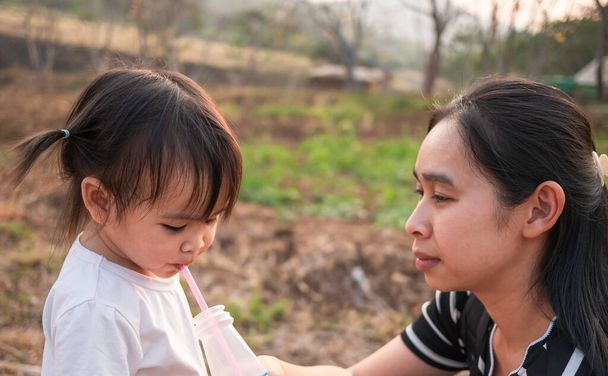 Malé asijské dítě dívka pít vodu z trubice poté, co unavený z hraní v zahradě s matkou - Fotografie, Obrázek