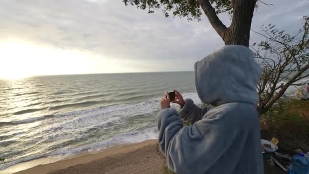 Жінка знімає або фотографує штормові моря з пляжу за допомогою мобільного телефону
. - Кадри, відео