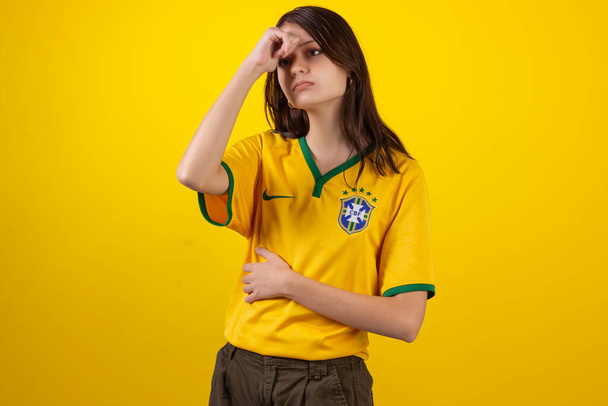 2022年のカタールカップでブラジルサッカーチームの公式ユニフォームを着た若い女性とスタジオ写真のブラジルの国旗。ブラジルのファン. - 写真・画像