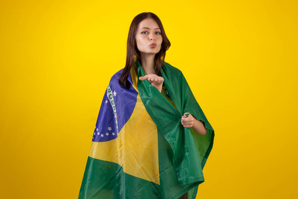 Mulher de salto usando a camisa oficial do time de futebol brasileiro na Copa do Qatar de 2022 e com a bandeira do Brasil em foto de estúdio. Fã brasileiro. - Foto, Imagem