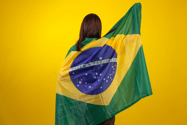 Montréalaise portant la chemise officielle de l'équipe brésilienne de football dans la Coupe Qatar 2022 et avec le drapeau du Brésil en photo studio. ventilateur brésilien. - Photo, image