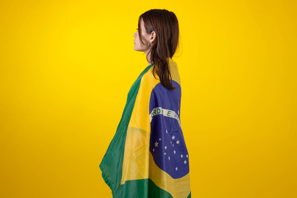 2022 Katar Kupası 'nda Brezilya futbol takımının resmi formasını giyen ve stüdyo fotoğrafında Brezilya bayrağı taşıyan bir kadın. Brezilyalı taraftar. - Fotoğraf, Görsel