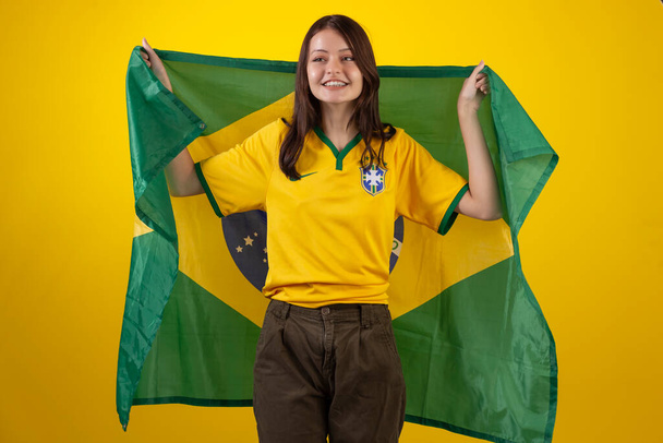 accompagnatrice che indossa la maglia ufficiale della squadra di calcio brasiliana nella Coppa del Qatar 2022 e con la bandiera del Brasile in foto in studio. Ventilatore brasiliano. - Foto, immagini