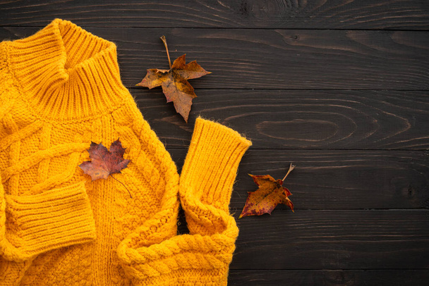 Cozy autumn background. Knitted sweater with fall leaves on wooden rustic background. Flat lay image. - Zdjęcie, obraz