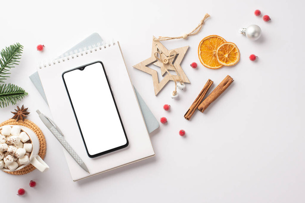 Top view φωτογραφία του χριστουγεννιάτικη διακόσμηση smartphone ημερολόγιο αστέρι ξύλο στολίδι φλιτζάνι κακάο με marshmallow fir κλαδί γκι κανέλα μπαστούνια αποξηραμένα φέτες εσπεριδοειδών σε απομονωμένο λευκό φόντο με copyspace - Φωτογραφία, εικόνα