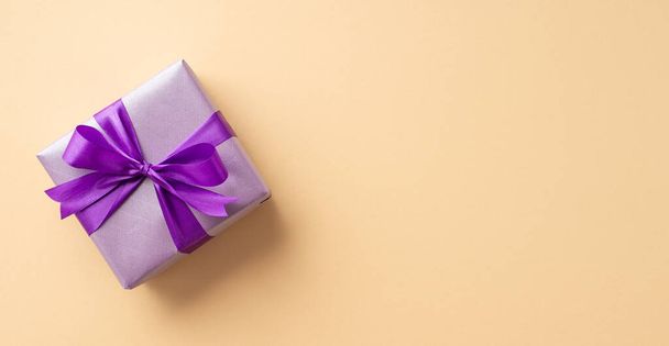 New Year concept. Top panoramic view photo of stylish lilac giftbox with violet ribbon bow on isolated pastel beige background with copyspace - Foto, Bild