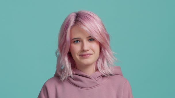 Fun confused shy shamed young hipster student girl 20s with pink hair look camera biting lips, say oops I am sorry, I do not know how it happened. Model feeling guilty blue background.People lifestyle - Footage, Video