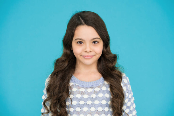 She is really cute. Happy girl child blue background. Small child wear long wavy hair. Little child with cute smile. Beauty salon. Fashion and style. Child care and childhood. - Foto, immagini