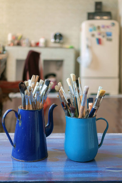 Verschiedene professionelle Pinsel im blauen Metallgefäß auf unscharfem Studiohintergrund, selektiver Fokus - Foto, Bild