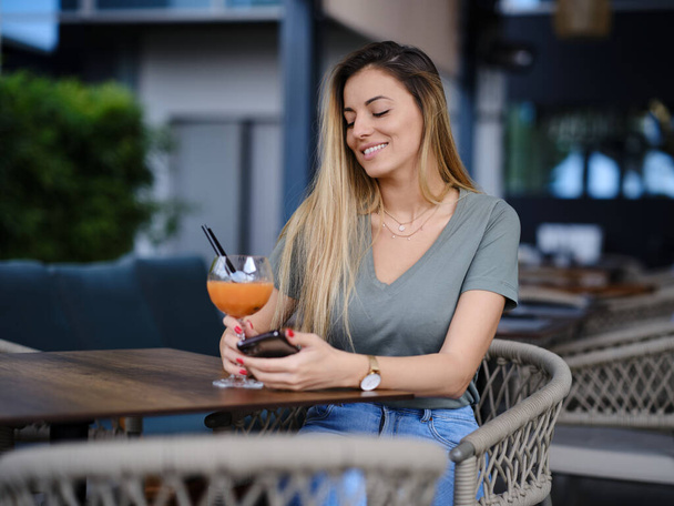 Счастливая молодая женщина сидит в баре и пьет коктейль. - Фото, изображение