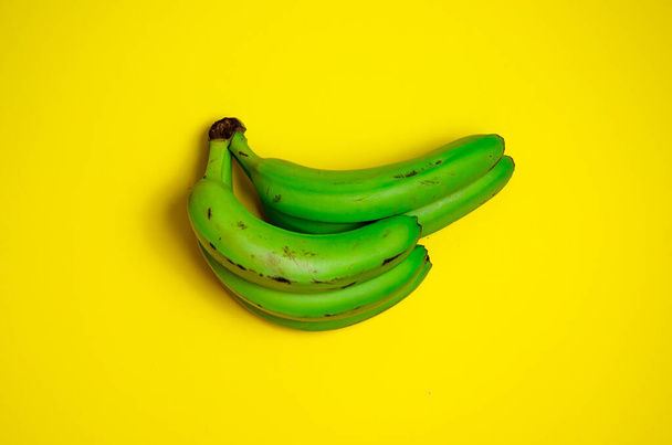 コピースペースのある黄色の背景のフラットレイアウトの緑のバナナ。醜い食べ物の概念 - 写真・画像