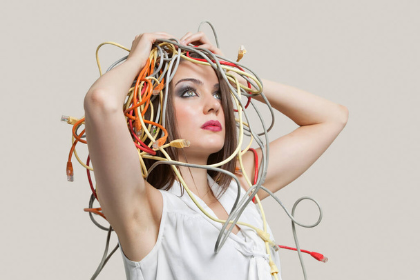 "Kafası gri arka planda renkli kablolara dolanmış genç bir kadın." - Fotoğraf, Görsel