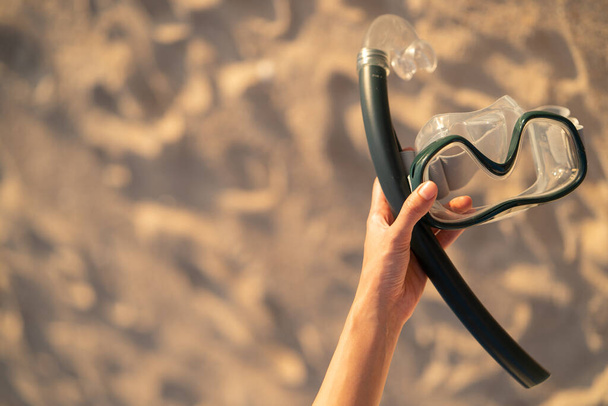 Hand met uitrusting voor snorkelen masker op het strand. - Foto, afbeelding