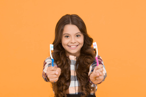 Twice faster. Girl cute long hair holds toothbrushes yellow background. Child girl holds two toothbrushes. Child school girl smart kid happy face cares hygiene. Brush teeth concept. Teeth hygiene. - Fotó, kép