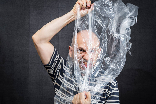 Homme mûr avec un sac en plastique transparent survolant sa tête et son visage. suffoquer. visage dans un sac plastique, strangulation - Photo, image