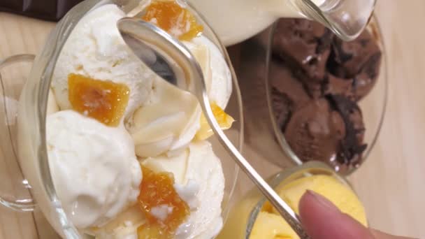 Vertical video. Three glass jars filled with ice cream balls with vanilla, chocolate, mango and banana flavors. A womans right hand is lowered with a teaspoon to take vanilla ice cream. - Footage, Video
