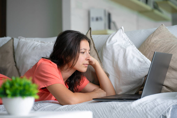 "ソファに寝そべっている女の子はノートパソコンを見て喜ぶ。笑顔, " - 写真・画像