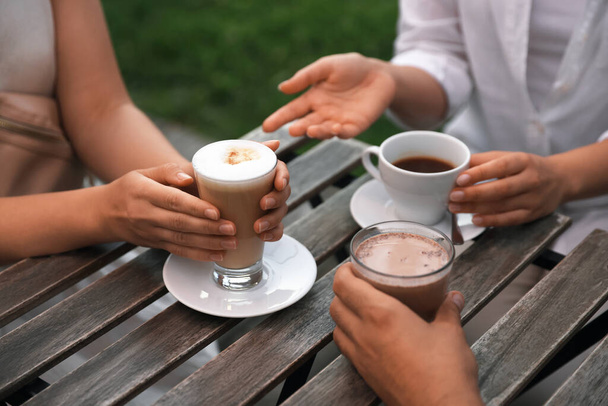 Friends drinking coffee and cocoa at wooden table in outdoor cafe, closeup - Foto, Bild