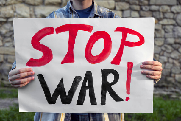 Woman holding poster with words Stop War against brick wall outdoors, closeup - Fotó, kép