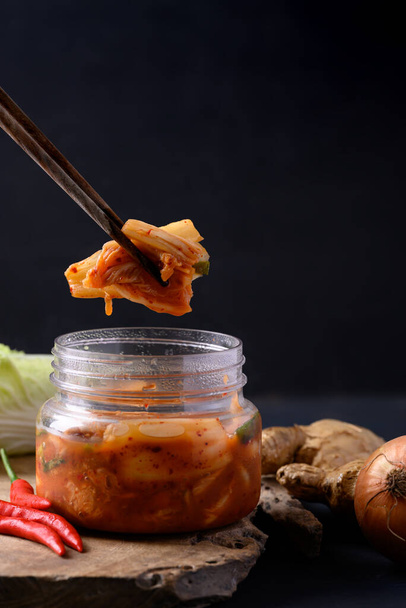 Капуста кимчи в миске едят палочками на черном фоне, азиатская ферментированная пища - Фото, изображение