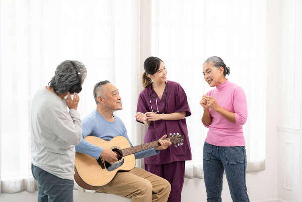 Ομάδα ηλικιωμένων που απολαμβάνουν τις δραστηριότητες μαζί με το γιατρό. Οι ηλικιωμένοι διασκεδάζουν. Ευτυχισμένος τελειόφοιτος παίζοντας κιθάρα και τραγουδώντας τραγούδια διασκεδάζοντας μαζί. - Φωτογραφία, εικόνα