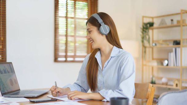 Negócio em casa conceito, Empresária usar fone de ouvido para reunião em videochamada e tomar notas. - Foto, Imagem