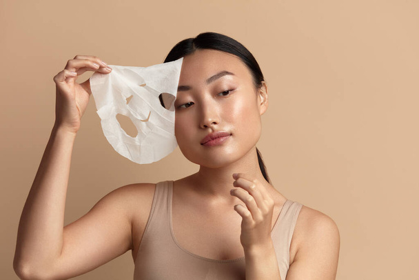 Beauty Woman Face Mask. Portrait Of Beautiful Girl Removing Sheet Mask from Healthy Fresh Skin. Closeup Of Attractive Woman With Natural Makeup And Mask On Facial Skin. High Resolution  - Foto, Bild