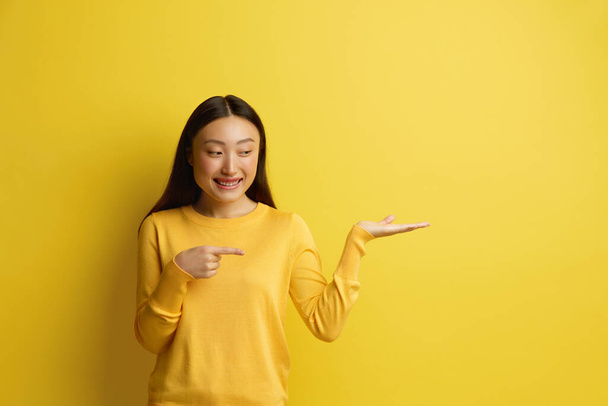 Smiling Woman Pointing Aside. Amused Young Girl Points Finger Away at the Empty Copy Space. Pretty Female Isolated on Yellow. Advertising Concept  - Foto, immagini