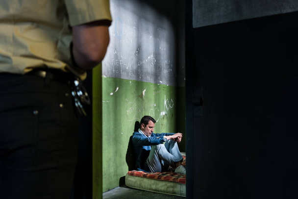 Młody więzień siedzi sam w przestarzałym strażniku więziennym - Zdjęcie, obraz