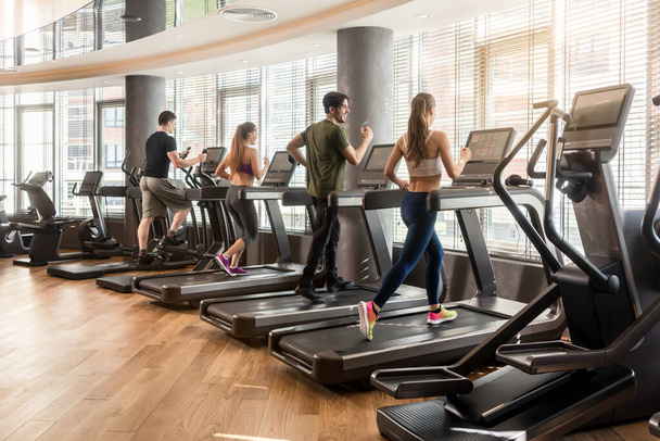 Groep van vier mensen lopen op de loopband in de fitness gym - Foto, afbeelding