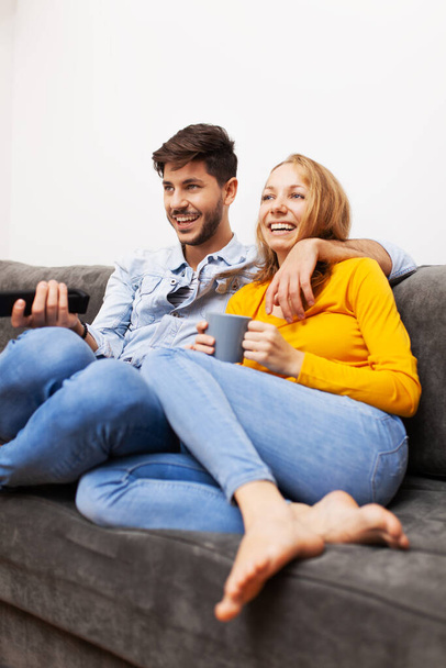 "ζευγάρι ερωτευμένο σε καναπέ στο σπίτι, βλέποντας τηλεόραση και χαμογελώντας " - Φωτογραφία, εικόνα