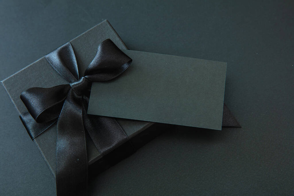 Чёрная пятница и рождественские подарки. Подарочная коробка с черной лентой и пустой картой изолированы на черном фоне, - Фото, изображение