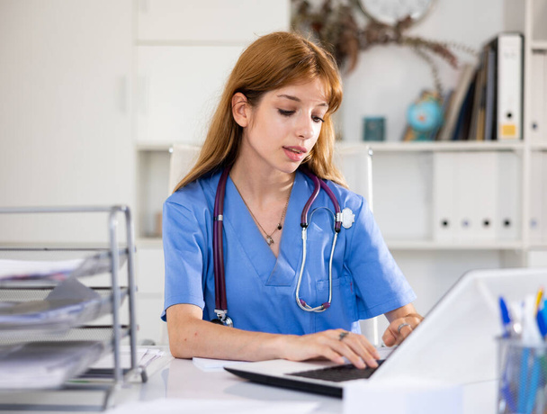Cheerful woman doctor sitting at workplace with computer in her office - Foto, Bild
