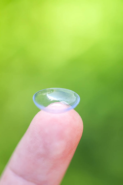 Transparente Kontaktlinse an der Fingerspitze auf verschwommenem grünen Sommer-Natur-Hintergrund - Foto, Bild