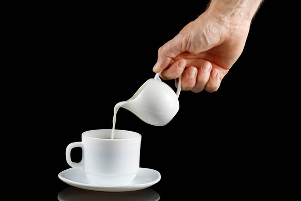 Kaffee mit Milch vorhanden. Milch wird in eine Tasse mit Kaffee gegossen. Milch zu einer Tasse Kaffee hinzufügen - Foto, Bild