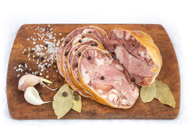 Румынское традиционное блюдо под названием тоба или пифти, приготовленное из свиных органов в натуральной мамбране, ломтики на деревянной доске с чесноком, лавровыми листьями и перцем. Изолированный на белом крупным планом - Фото, изображение