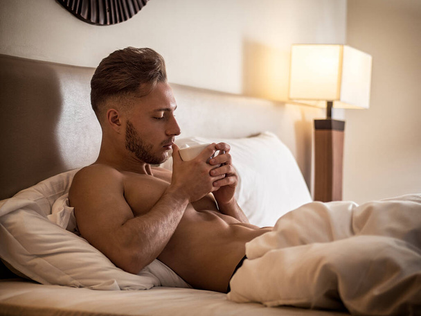 "Sexy naked young man on bed with cup" - Foto, afbeelding