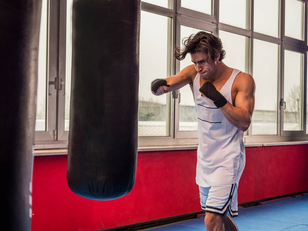 Muscular sportive man training with punching bag while boxing - Photo, Image