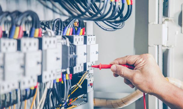 Ingeniero eléctrico prueba el funcionamiento del armario de control eléctrico sobre una base regular para el mantenimiento. - Foto, imagen