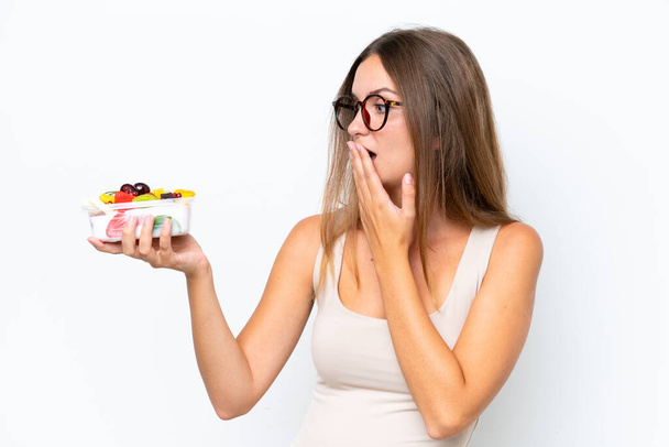 Mladá hezká žena drží misku ovoce izolované na bílém pozadí s překvapením a šokovaný výraz obličeje - Fotografie, Obrázek